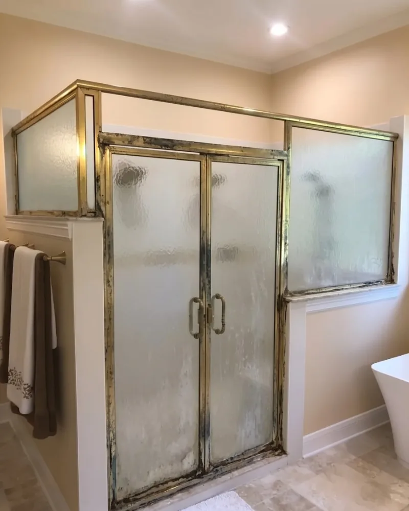 Before: Dated framed shower door with heavy aluminum trim and obscured glass